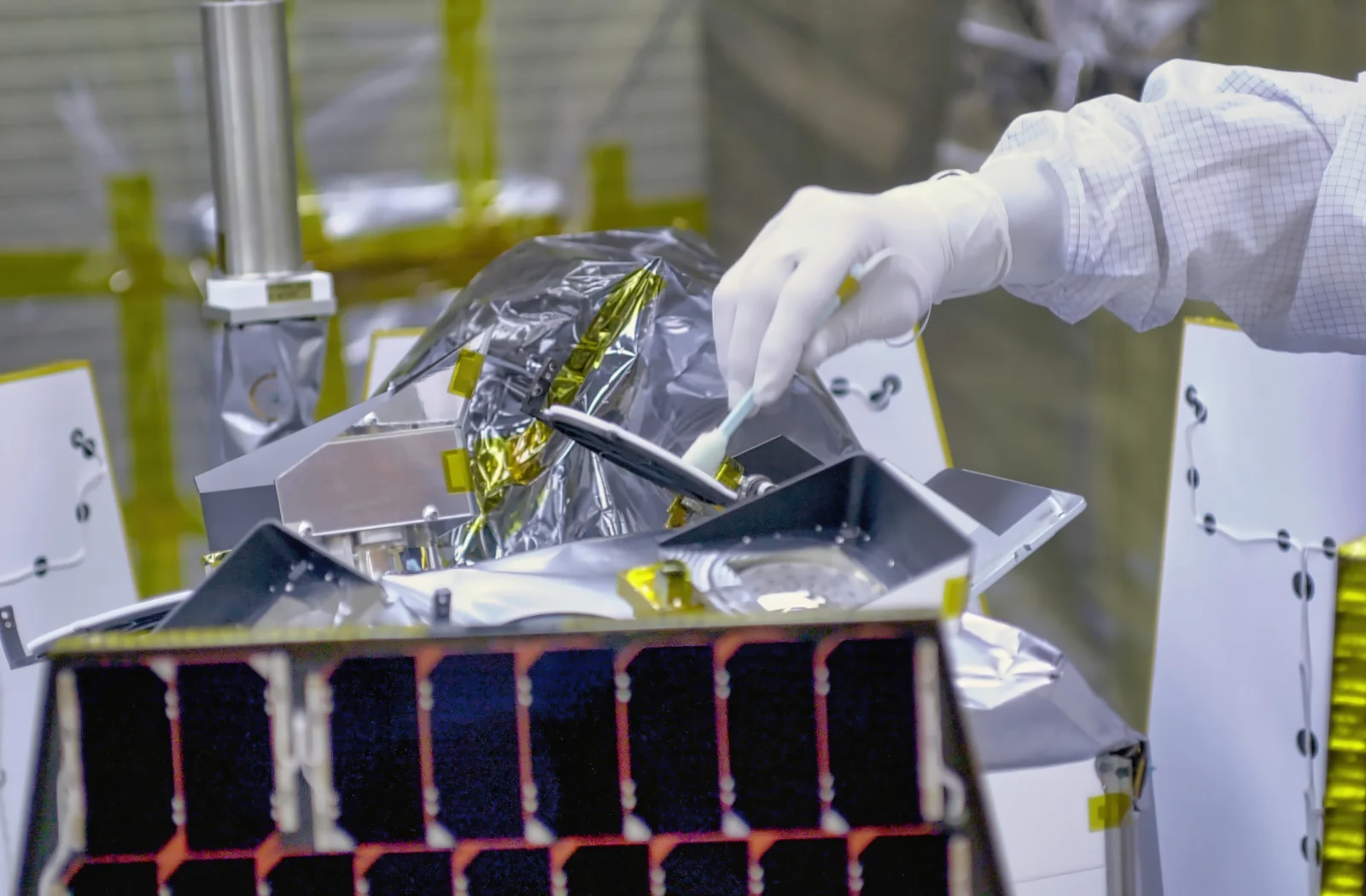 Technician in cleanroom gloves assembling a satellite structure