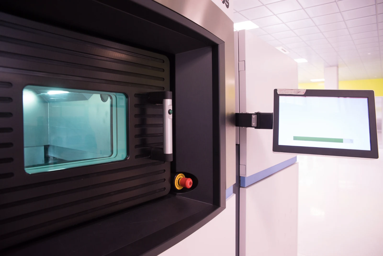 A large industrial printer enclosure with a lit viewing window and a control screen beside it.