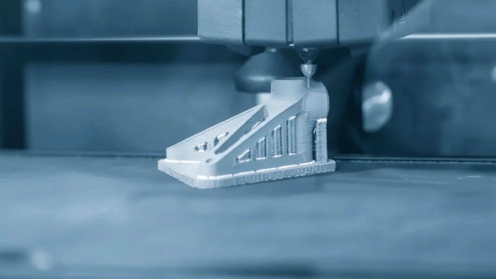 A metal bracket being built layer by layer under a printer nozzle.
