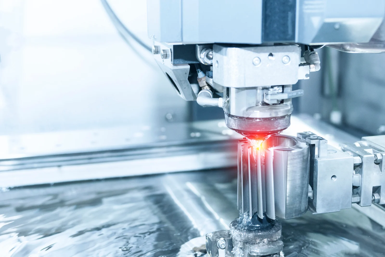 Wire EDM cutting a metal part under coolant with a glowing spark line